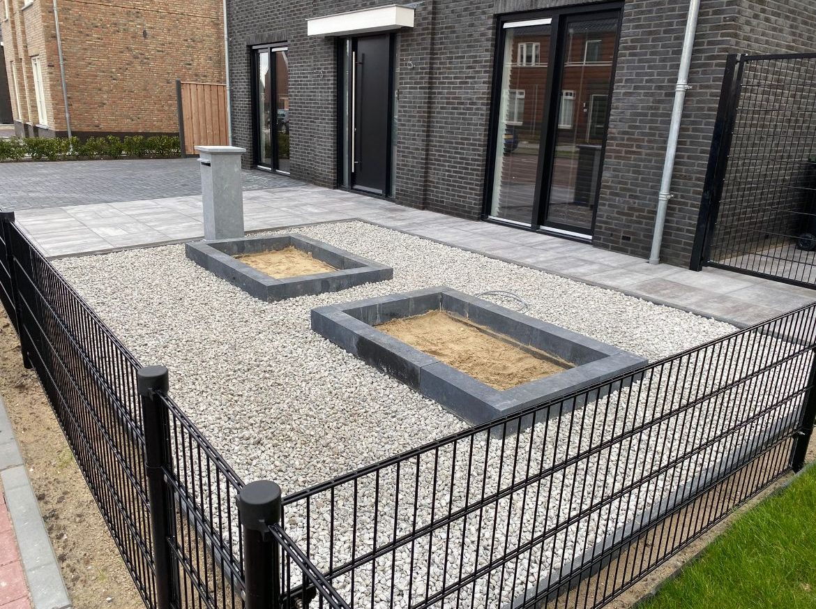 Voortuin met grind, twee betonnen plantenbakken en tegelpad
